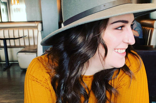 close-up photo of a woman wearing an orange top and a grey hat looking off to the side and smiling