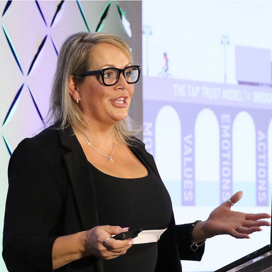 Woman giving a presentation with a screen behind her showing the TAP Trust Bridge Model