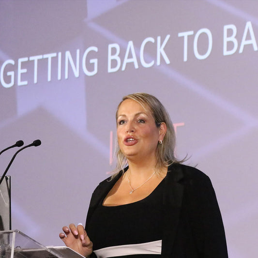 Woman giving a speech with 'Getting Back to Basics' text on screen behind her