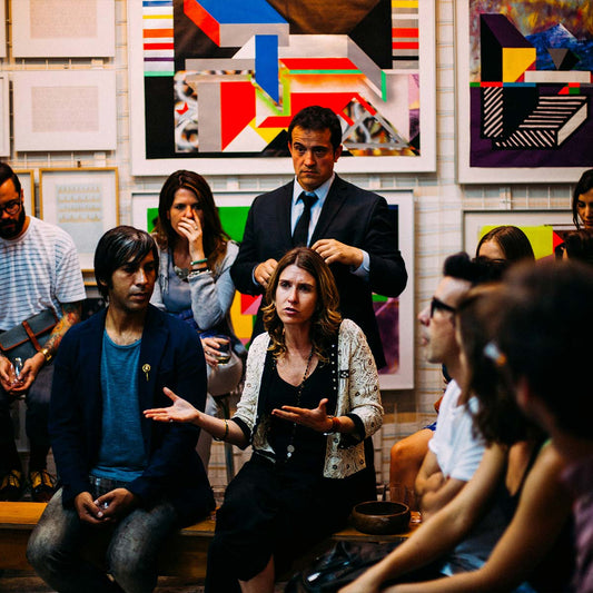 A group of diverse people sitting and standing in a half circle, deep in discussion being led by a woman