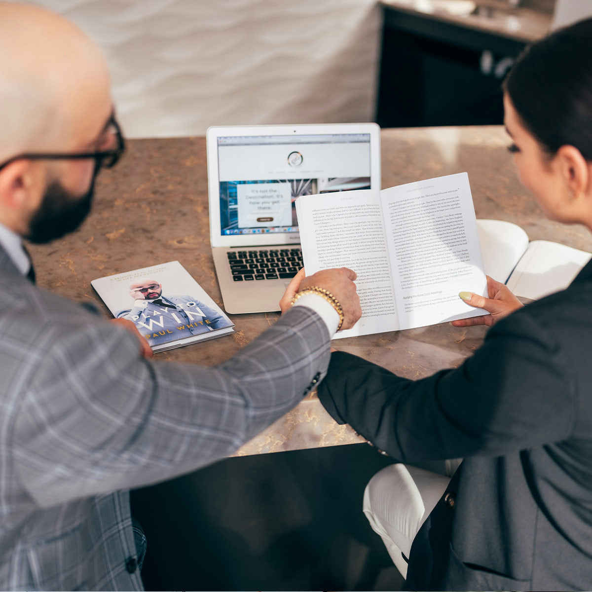 Two people sitting at a table with a laptop and documents