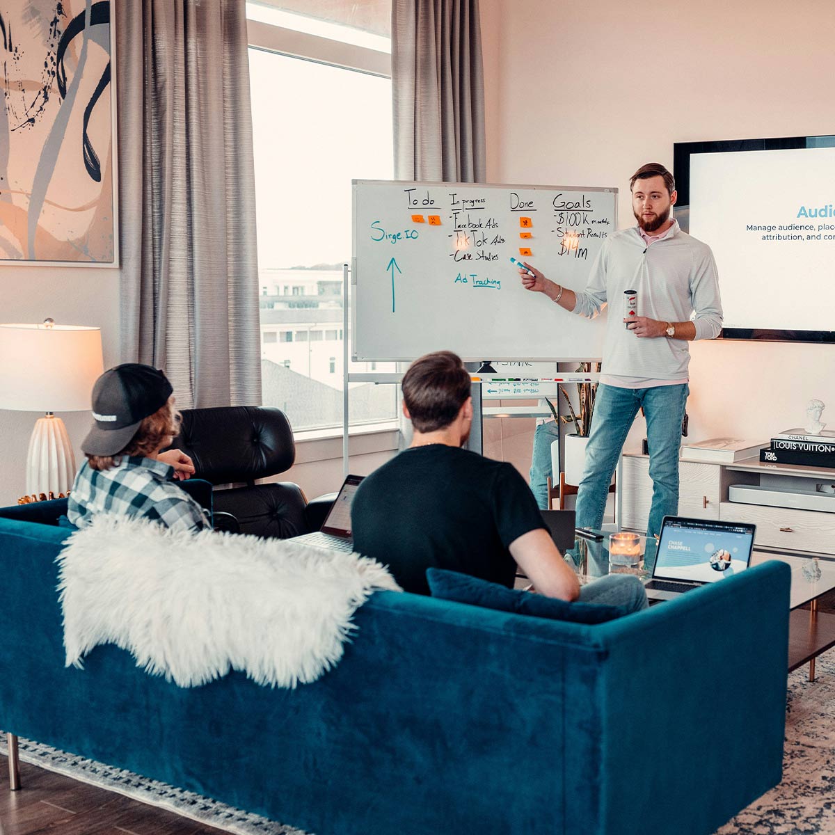 Person giving a presentation in a living room with a whiteboard and laptop.