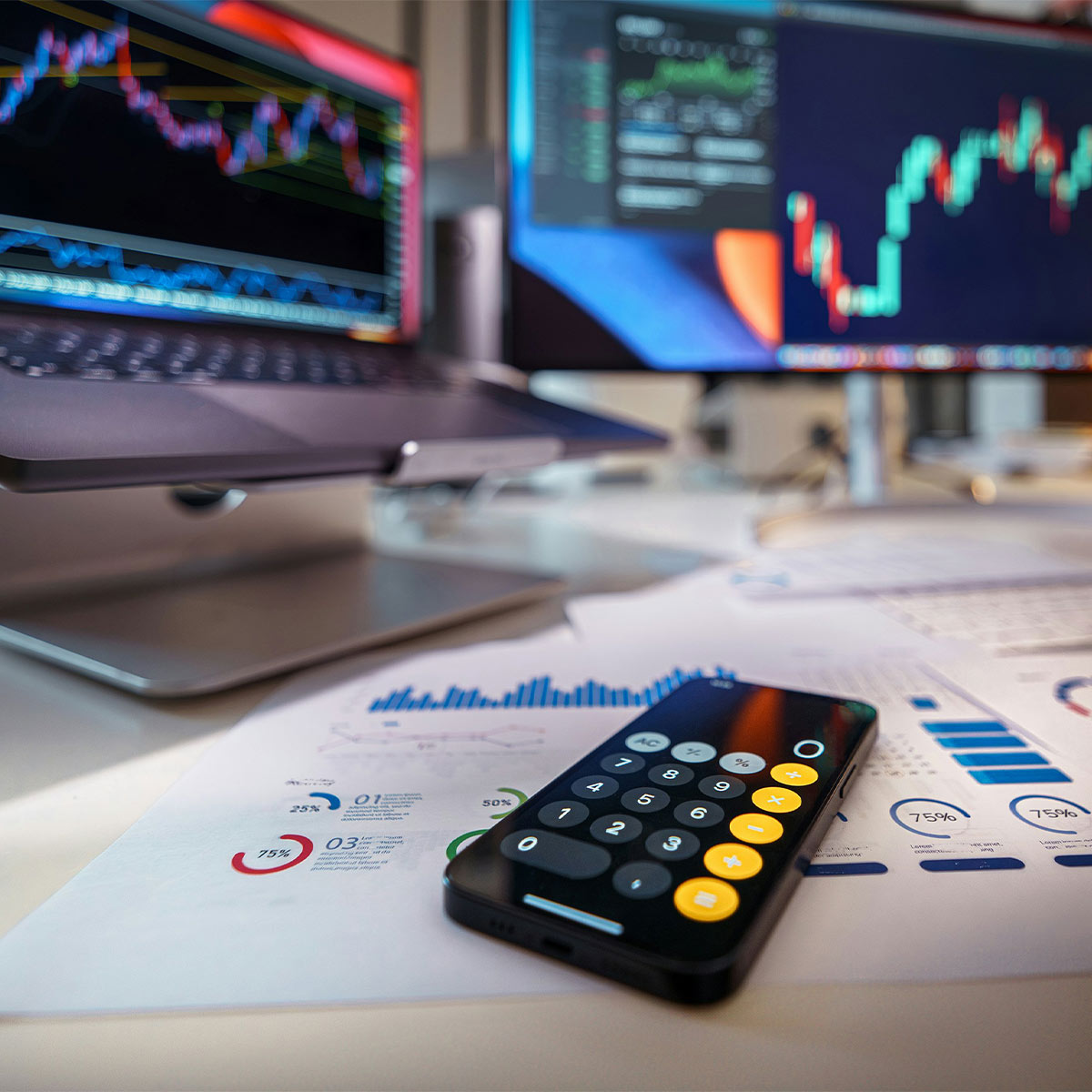 Phone on financial documents with computer screens displaying stock analytics and graphs in the background