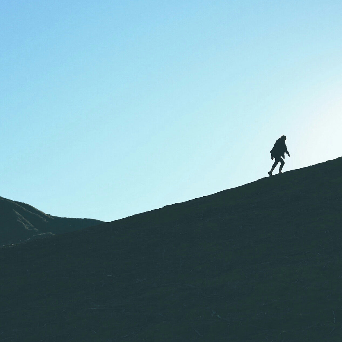 Silhouette of a person walking on a hill against a clear blue sky