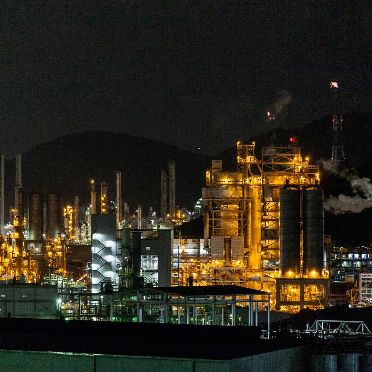 Industrial complex with illuminated structures against a dark night sky.