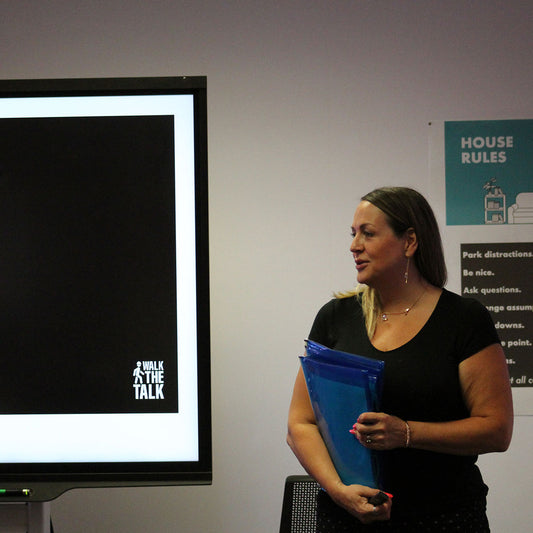 Woman holding a blue folder in front of a screen with 'Walk the Talk' logo.