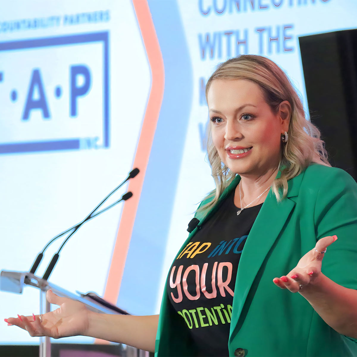 Shannon Rheault in green blazer and colorful shirt speaking at a conference with TAP branding.