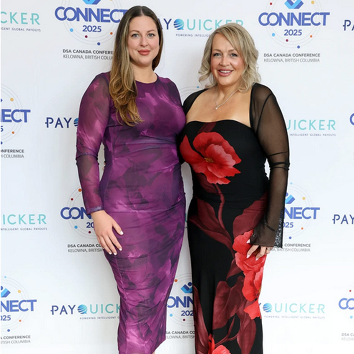Two women posing together at an event with a branded backdrop