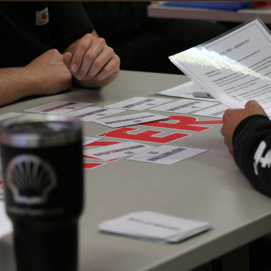 Two people sitting at a table with printed activity materials and a Shell-branded cup.