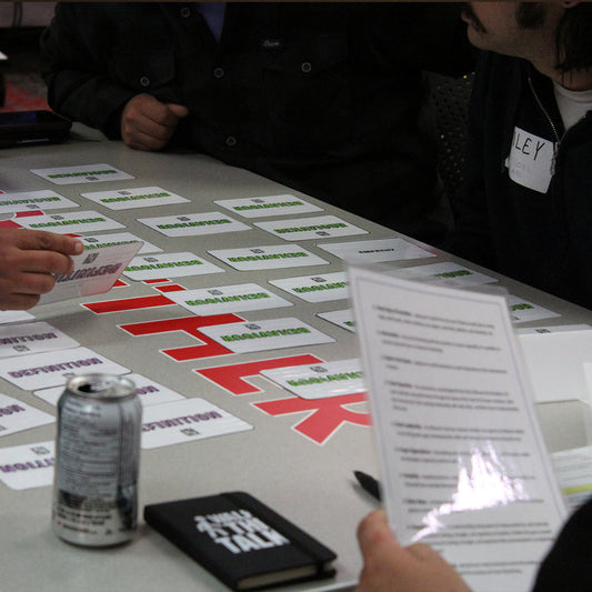 People around a table with cards, a can, and a book