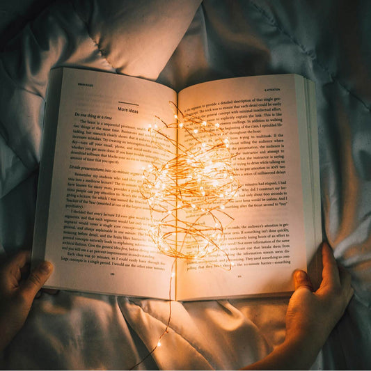 Open book held by hands with string lights inside, on a soft fabric background