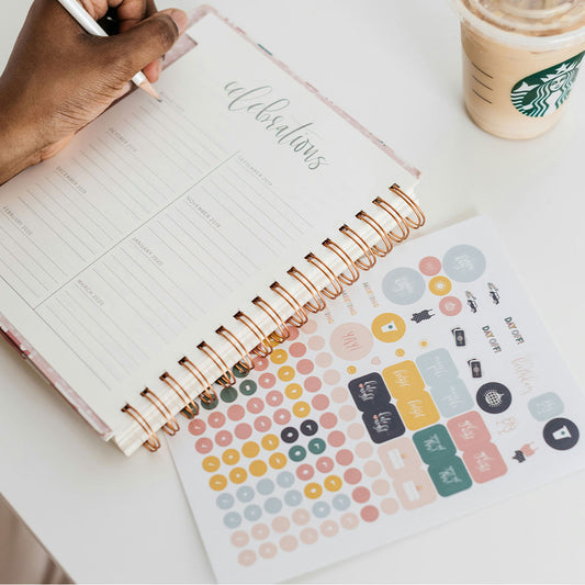 Open planner with stickers and a Starbucks cup on a white surface