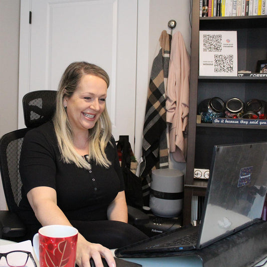 Woman smiling and sitting at a desk with a laptop, holding a red mug, in an office setting.