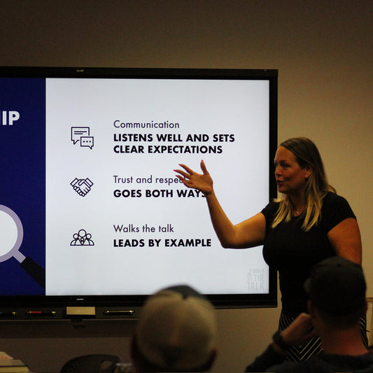 Woman giving a presentation with a screen that reads "Communication: Listens well and sets clear Expectations. Trust and Respect: Goes both ways. Walks the talk: Leads by example."