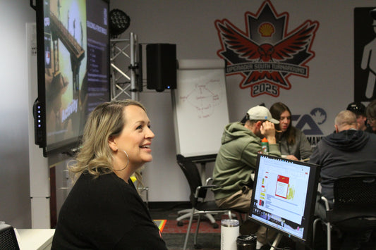a woman sitting in the front of the classroom smiling up at a student she is talking to 