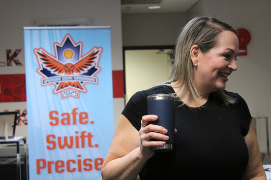 a woman standing in a classroom looking off to the side while smiling, a sign behind her reads: Safe. Swift. Precise.