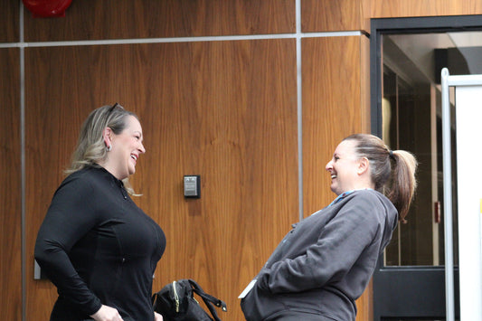 two blonde women standing in a board room chatting and laughing