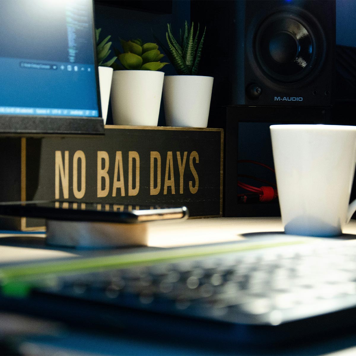 Desk setup with 'No Bad Days' sign, laptop, mug, and speakers.