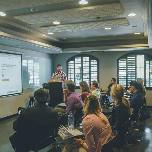 A classroom of adults sitting in front of a projector with a man standing at the front of the room while teaching 