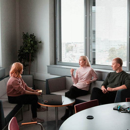 Three people sitting in a modern office setting with large windows.