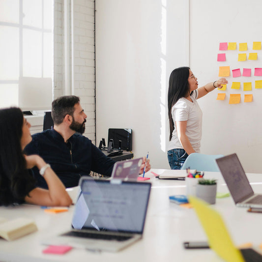 People working in a modern office with laptops and sticky notes on a whiteboard.
