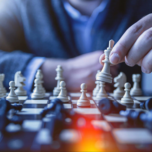 Person playing chess with a close-up of a hand moving a white chess piece.
