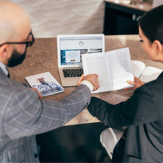 Two people sitting at a table with a laptop and documents