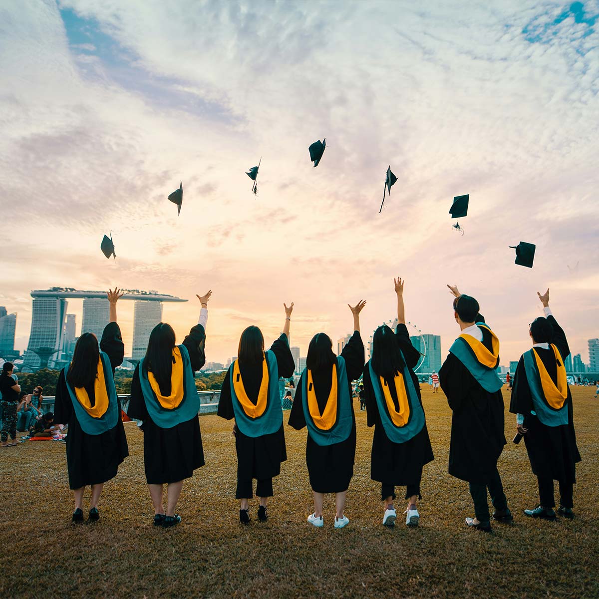 Graduates in caps and gowns throwing hats against a city skyline with a sunset.