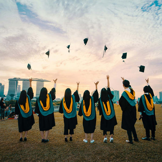 Graduates in caps and gowns throwing hats against a city skyline with a sunset.