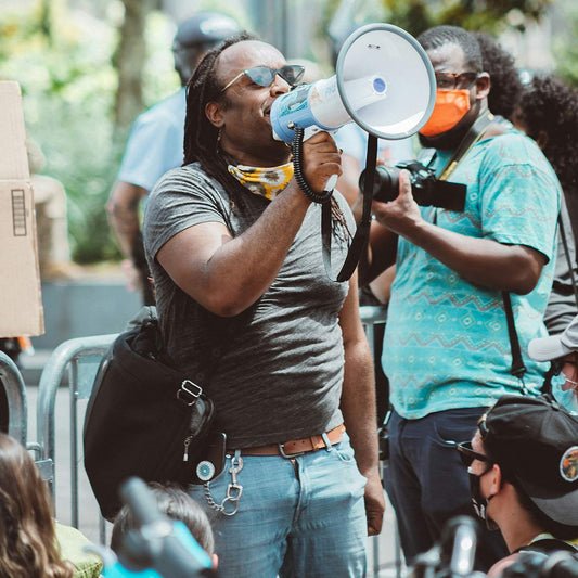 Person holding a megaphone in an outdoor setting with other people around