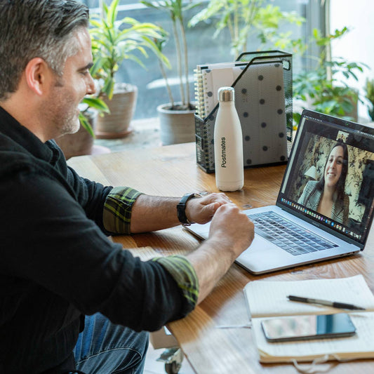 Man on a video call with a woman on a laptop at a desk with plants in the background