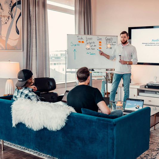 Person giving a presentation in a living room with a whiteboard and laptop.
