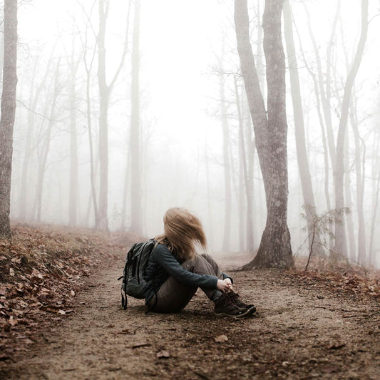 Person looking lost while sitting on a path in a foggy forest