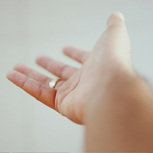 Hand wearing a gold ring, reaching out on a plain background