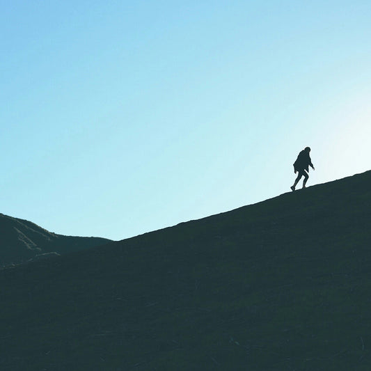 Silhouette of a person walking on a hill against a clear blue sky