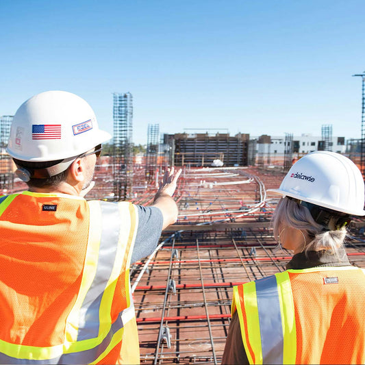 Two construction workers in hard hats and safety vests at a construction site.