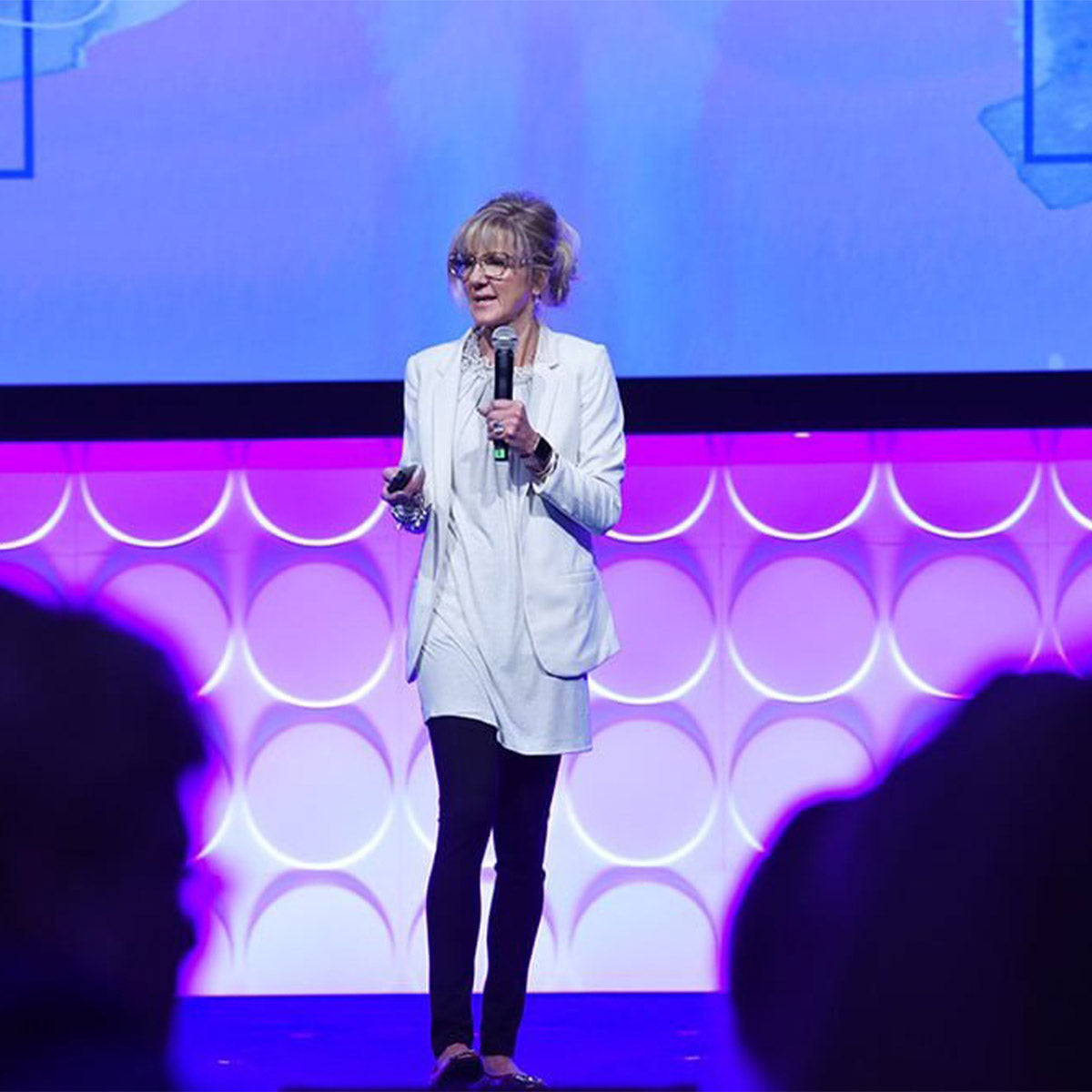 Woman on stage with a microphone against a colorful background