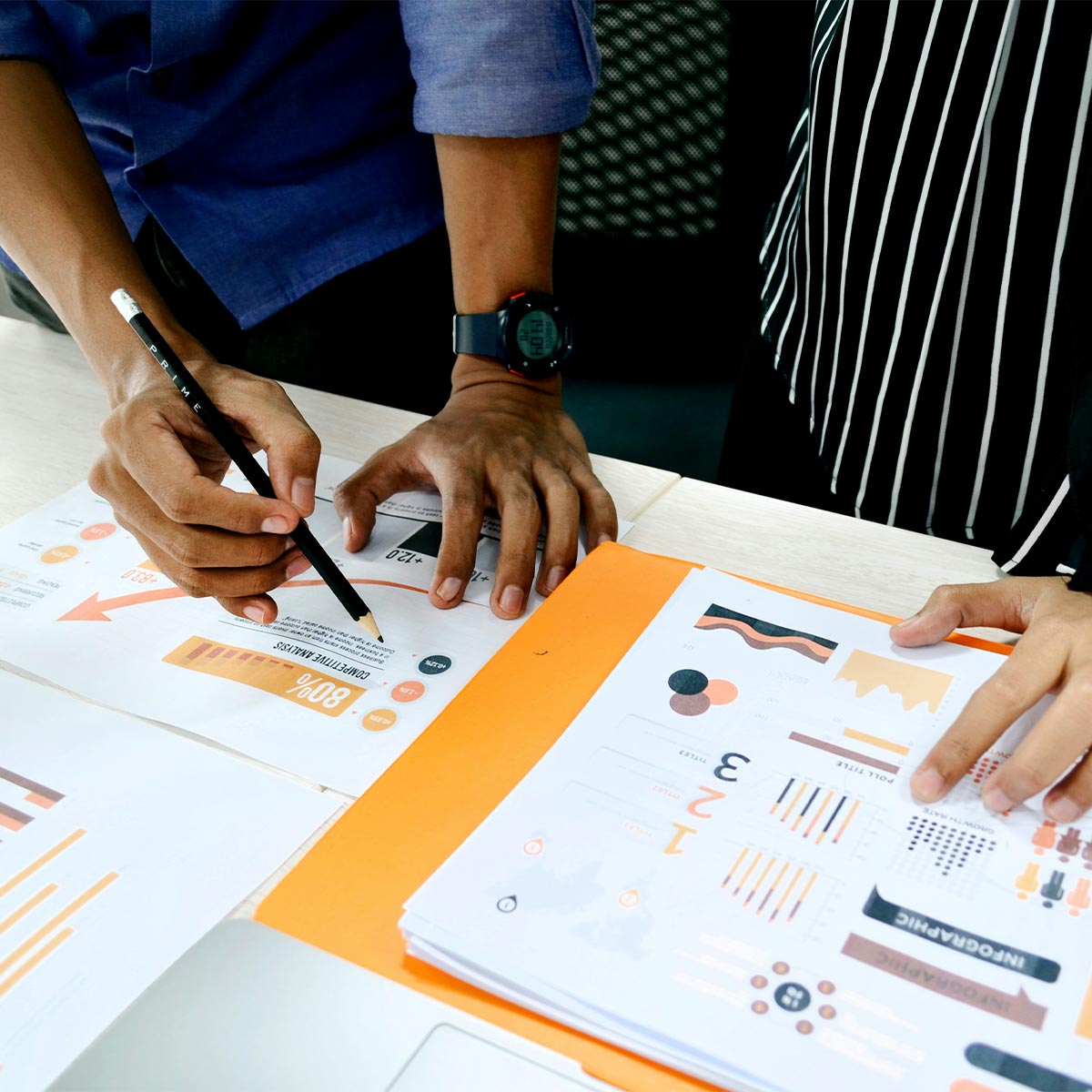 Two people working on a project with printed materials and a pencil.