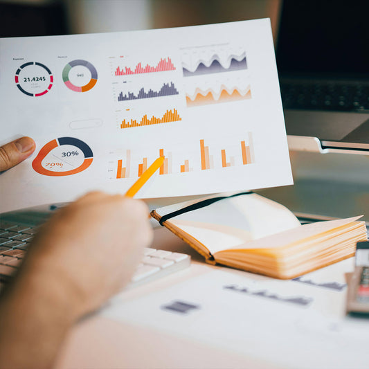 Person holding a sheet of paper with financial charts and graphs on a desk.