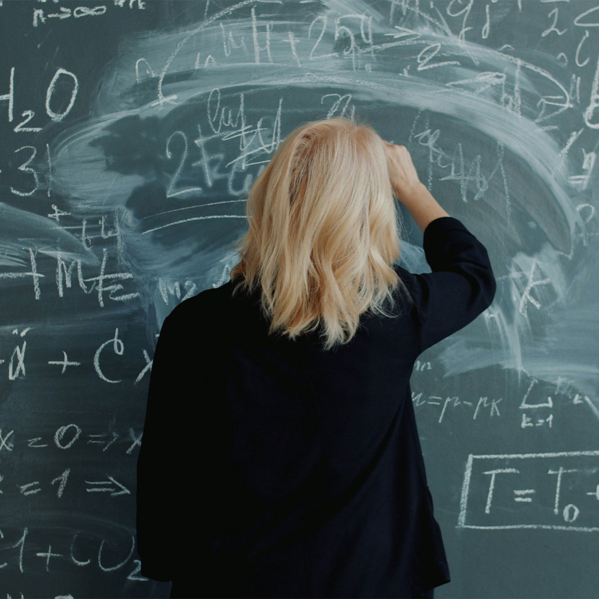 Person writing on a chalkboard filled with mathematical equations
