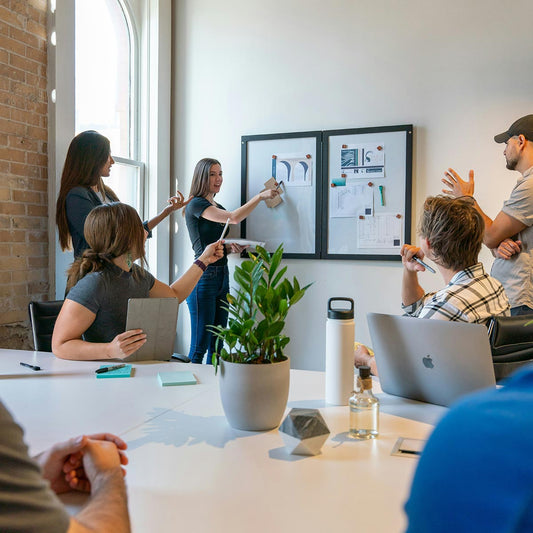 Group of people in a meeting room with a whiteboard and laptop.