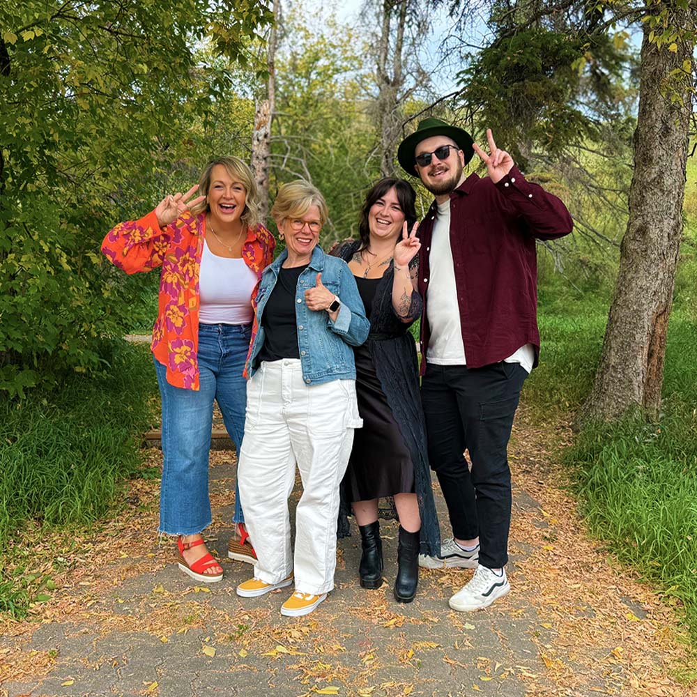 Four people posing on a path in a park with trees and greenery.