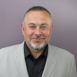 Man wearing a gray suit and black shirt against a purple background
